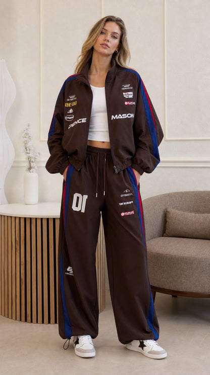 Front view of woman wearing brown retro racing tracksuit with zip jacket and wide-leg pants