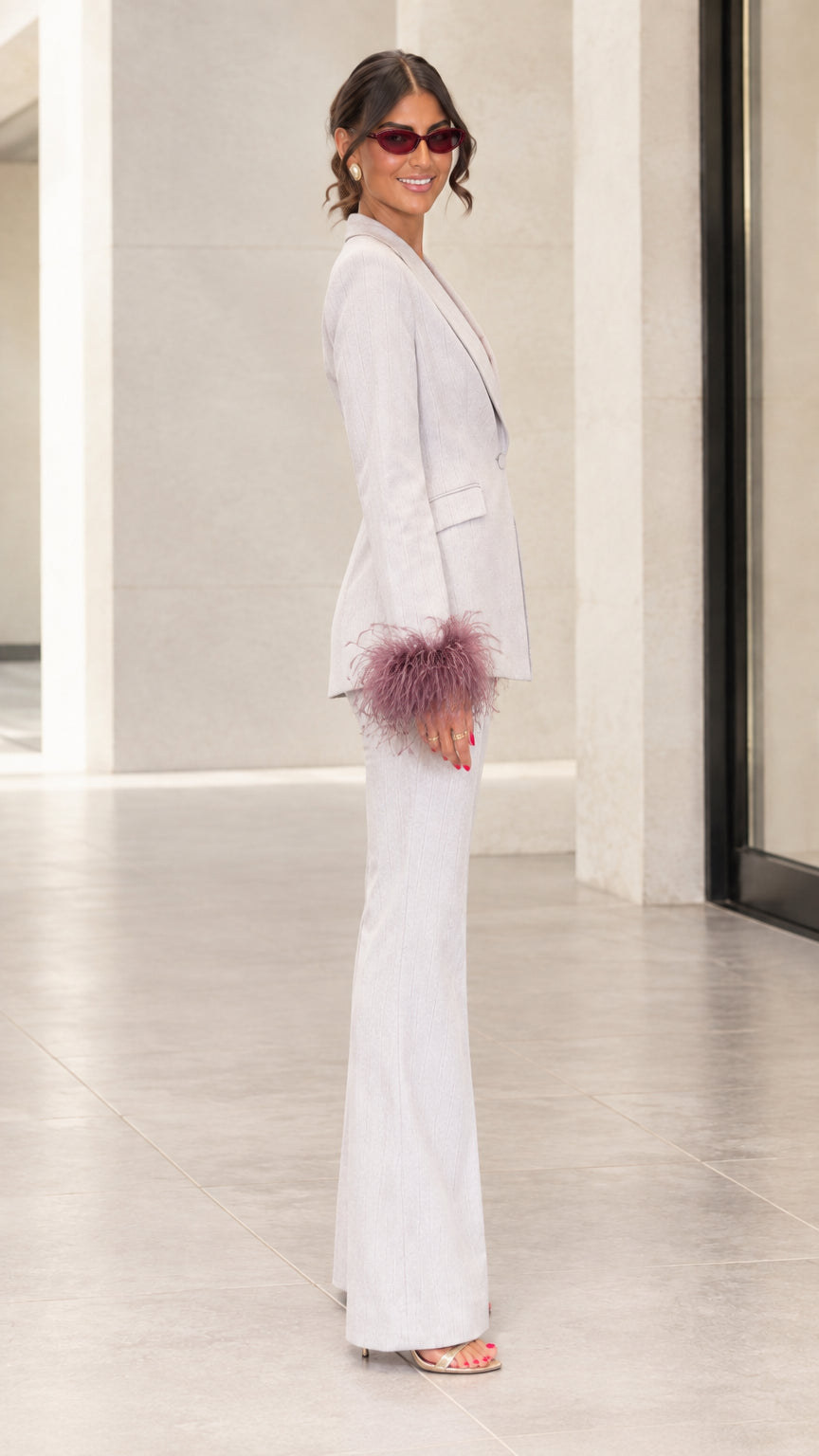 Side profile view of woman modeling light grey blazer with feather cuffs and matching trousers