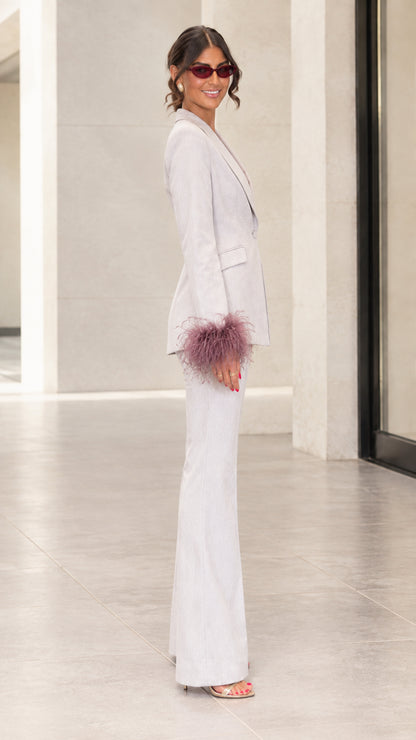 Side profile view of woman modeling light grey blazer with feather cuffs and matching trousers