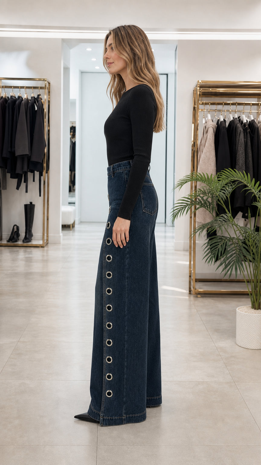 Side angle view of dark blue wide leg denim pants showing metallic eyelet row along the side