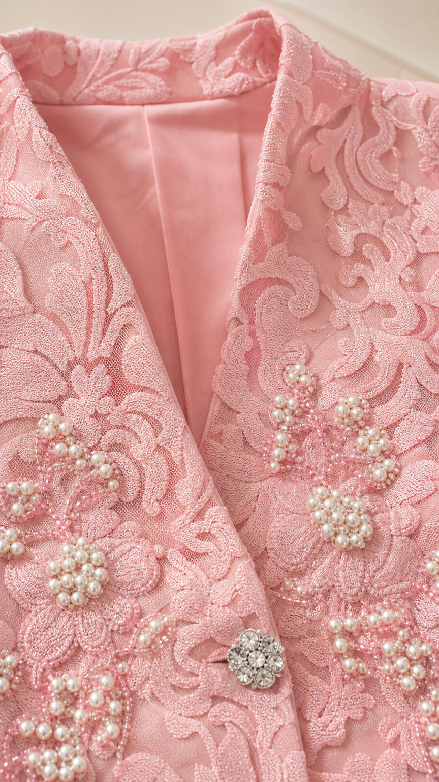 Close-up detail of pink lace jacket collar, faux pearl beading, and rhinestone button