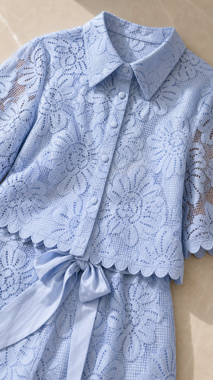 Close-up detail of light blue floral lace fabric, collar, covered buttons, and scalloped hem