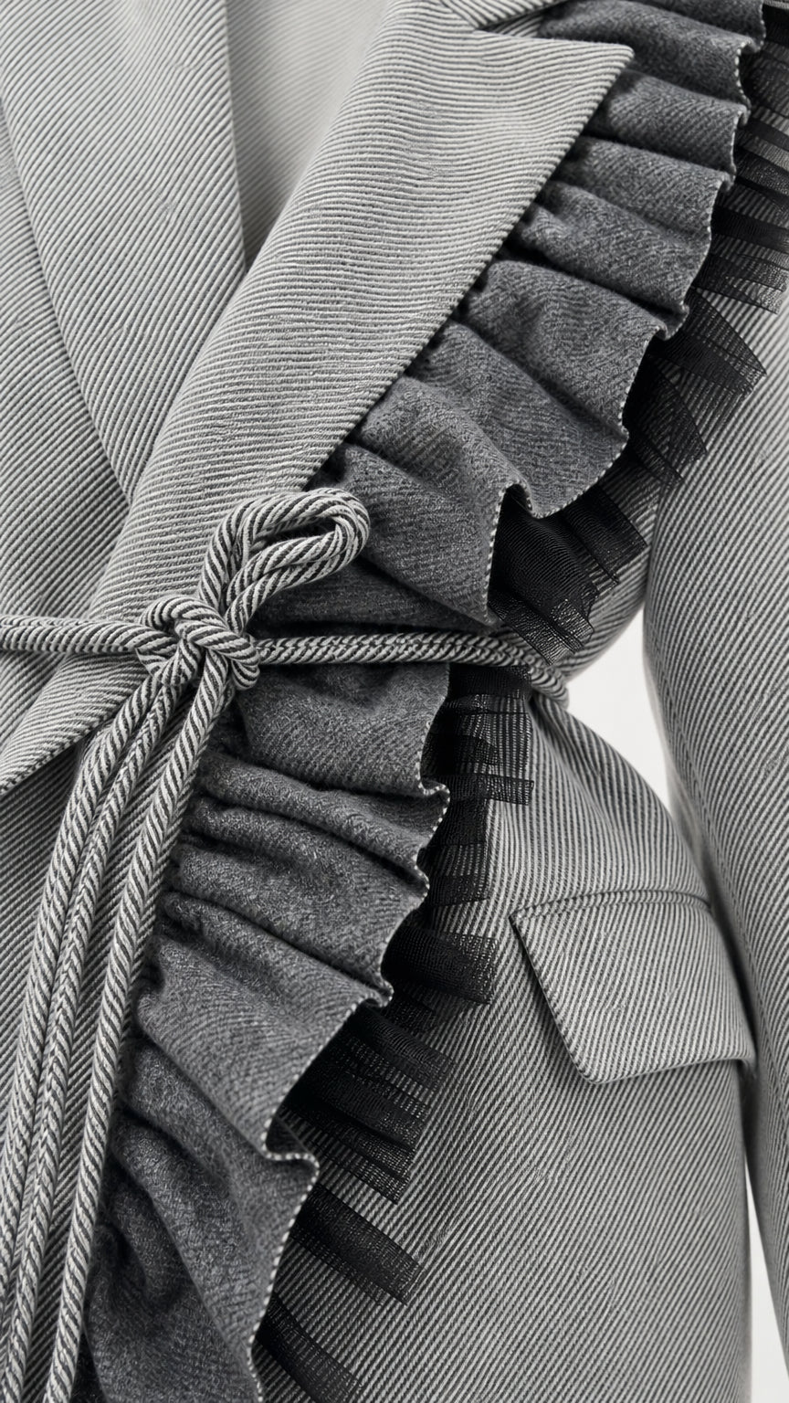 Close-up detail of grey twill suiting fabric with ruffled trim and braided cord belt