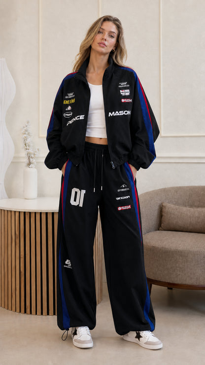 Full front view of woman wearing black retro racing jacket and matching track pants set