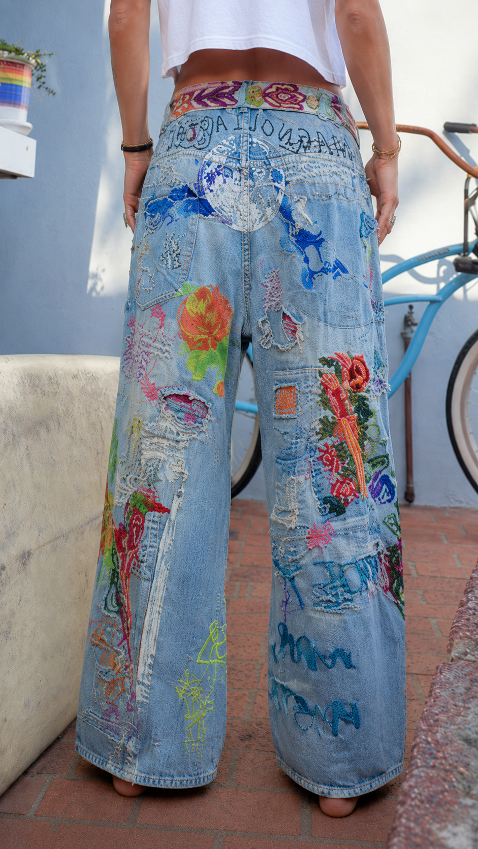 Back view of light blue patchwork jeans showing wide leg silhouette and rear artwork details