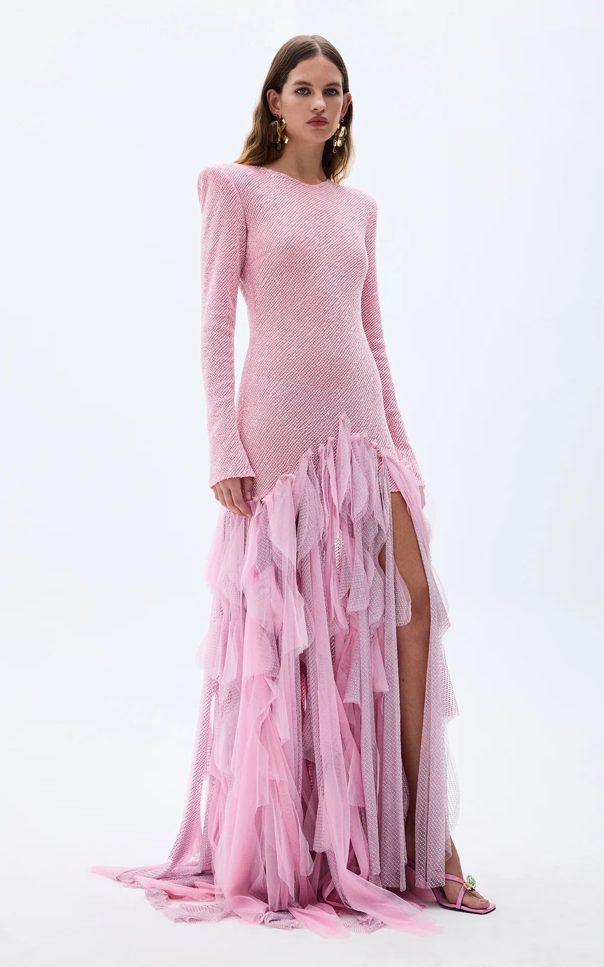 Angled front view of blush pink textured formal gown with long sleeves and high slit effect through ruffle hem