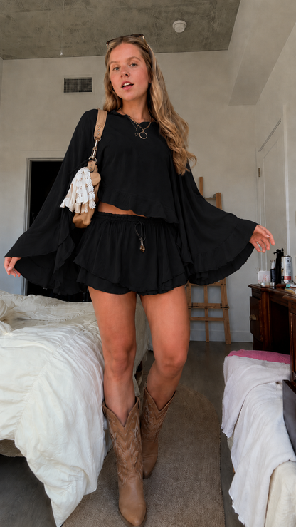 Front view of black bell sleeve crop top and matching ruffle skort set